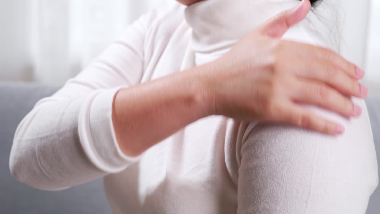 통증을 완화하고 휴식을 취하기 위해 어깨와 팔에 셀프 마사지를 하는 소파에 앉아 있는 여성을 닫습니다