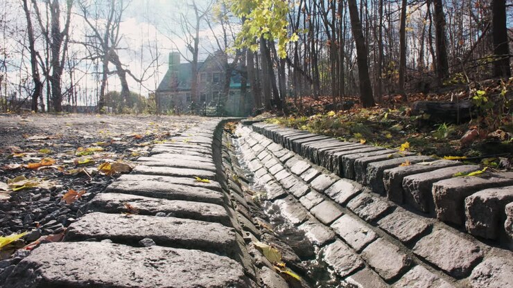 L'acqua piovana scorre giù da una storica grondaia in ciottoli nel Parco Mount Royal, con la luce del sole che luccica sulle pietre bagnate