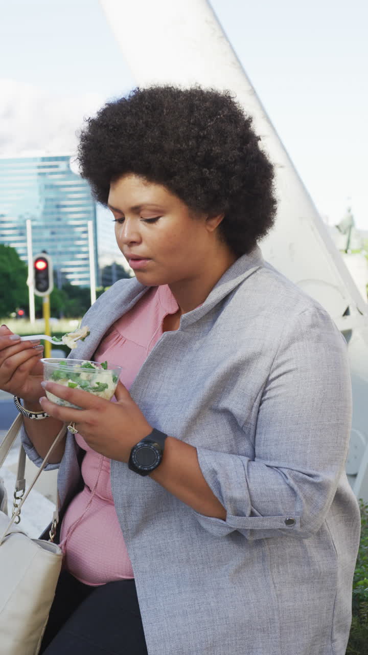 Vertical video of happy plus size biracial woman eating lunch on street