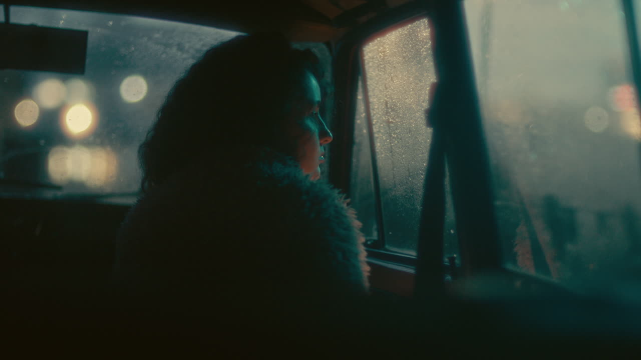 Young Woman Sitting in Car, Looking through Fogged Window in Evening