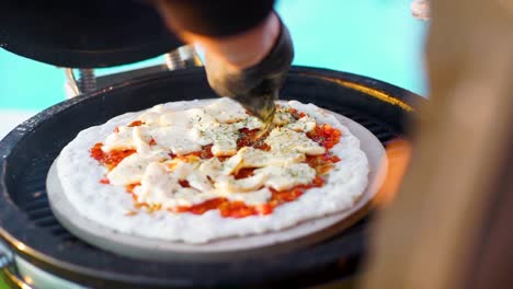 chef hand sprinkling oregano on pizza grilling outdoors