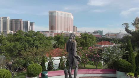 Órbita-Alrededor-De-La-Estatua-En-Carmel-Garden-Macao-Con-Horizonte-De-Casino-En-Segundo-Plano.