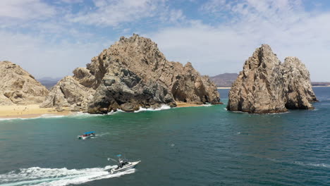 Wide-drone-shot-of-boats-in-the-ocean-with-sea-cliffs-in-the-background-in-Cabo-San-Lucas-Mexico,-rotating