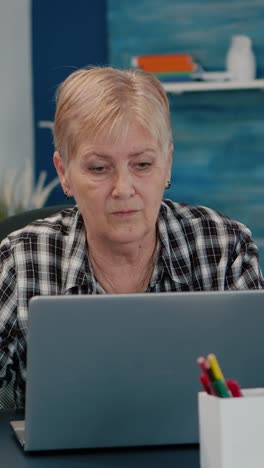Vertical video: Old middle aged businesswoman working at laptop from home
