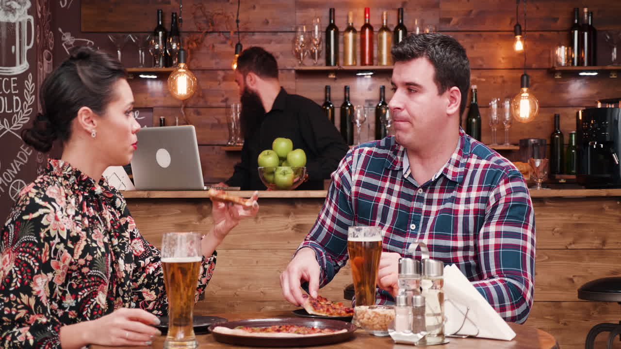 Couple Eating Pizza and Drinking Beer at a Restaurant