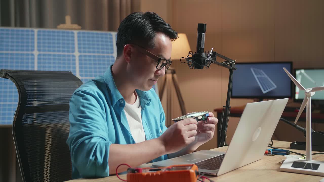 사무실에서 태양전지 에 노트북으로 작업하는 동안 회로판을 보는 풍력 터빈을 가진 아시아인