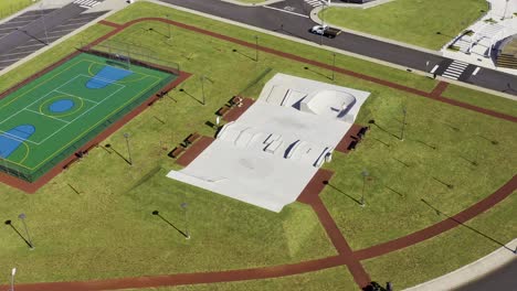 drone-footage-of-concrete-skate-park-surrounded-by-green-grass-and-sports-field-in-Velas,-Sao-Jorge-island,-Azores,-Portugal