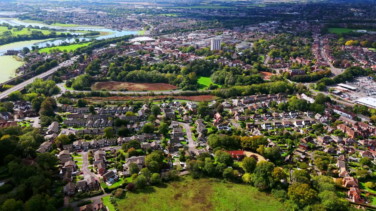 Aerial drone flies over Fareham, England, capturing trees, river, roads, and suburban houses surrounded by autumn colours glowing warmly in golden sunset light across the scenic landscape