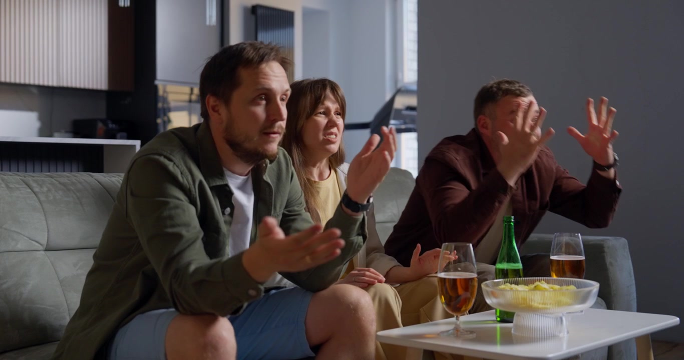 Venner ser tv derhjemme og reagerer med skuffelse.