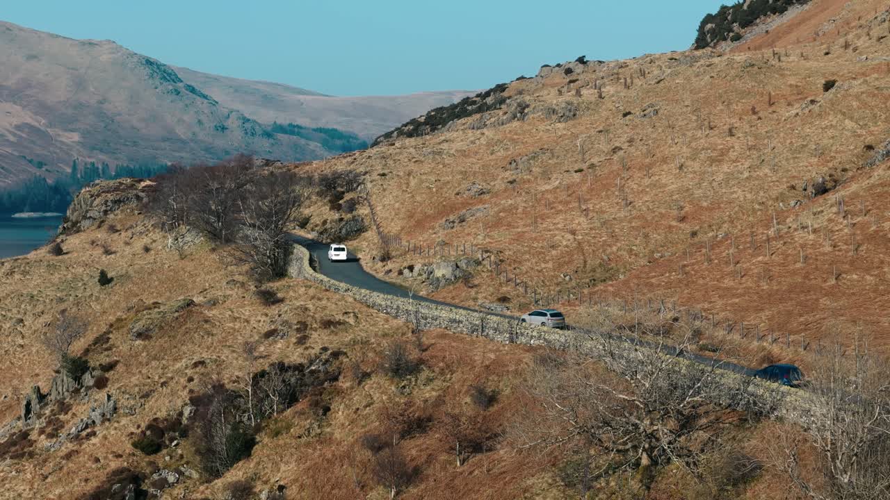 Tracking aerial of car driving through Lake District farmland in spring light, exploration and tourism