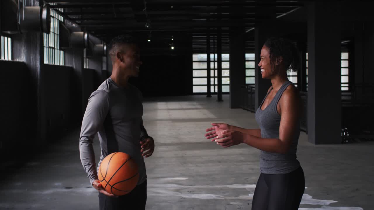 African american man and woman standing in an empty building playing with a basketball