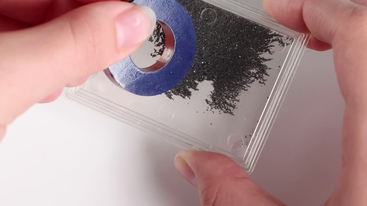 A ring magnet interacts with iron filings, demonstrating magnetic patterns on a clear surface.