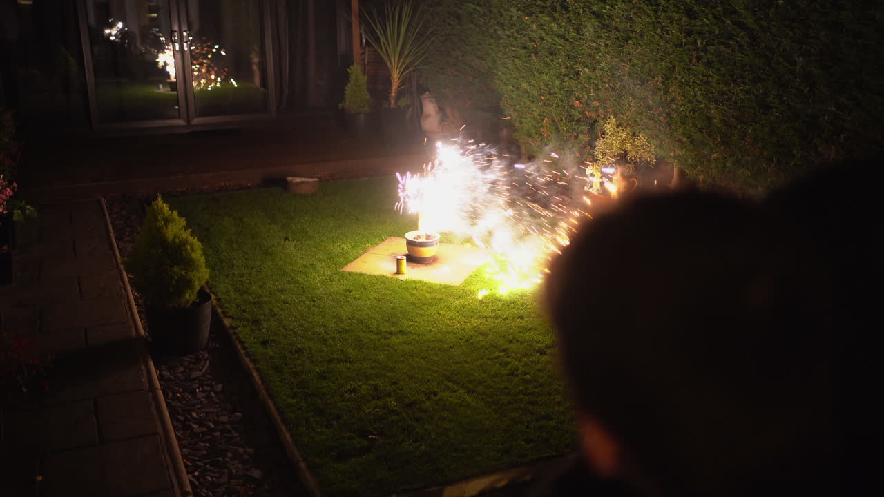 어둠 속에서 스파크와 밝은 색상으로 바람 부는 뒷마당에서 불꽃놀이 그림자 실루엣으로 멀리서 지켜보는 한 사람