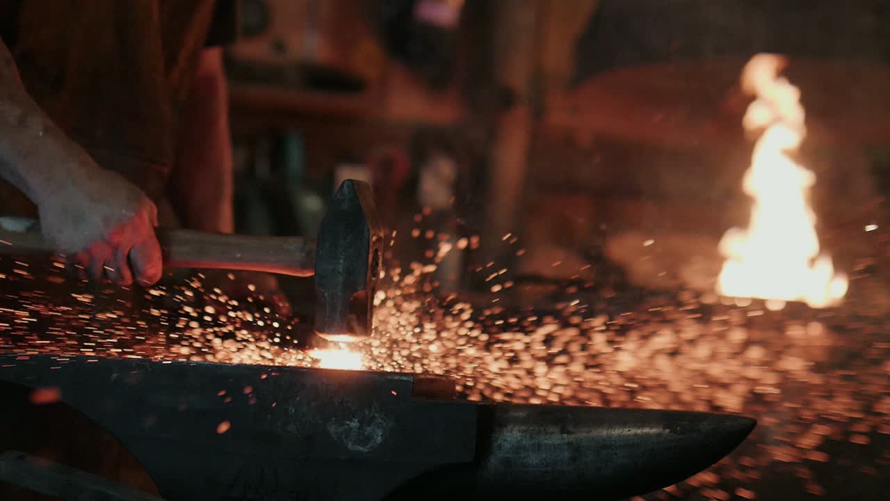 A blacksmith slams his hammer down on the anvil