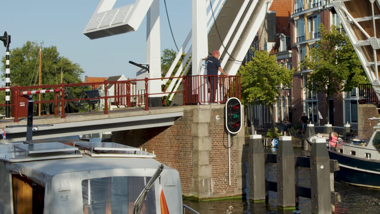 Bascule drawbridge lifts for motorboat on Haarlem canal, Netherlands, with historic cityscape in daylight