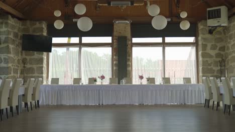 tables set up for a wedding feast at the venue, adorned with white decorations and ready for guests, with no people present.