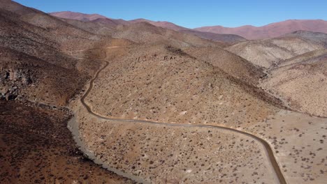 Rough-arid-hilly-landscape-aerial:-Serpentine-dirt-road-winds-through