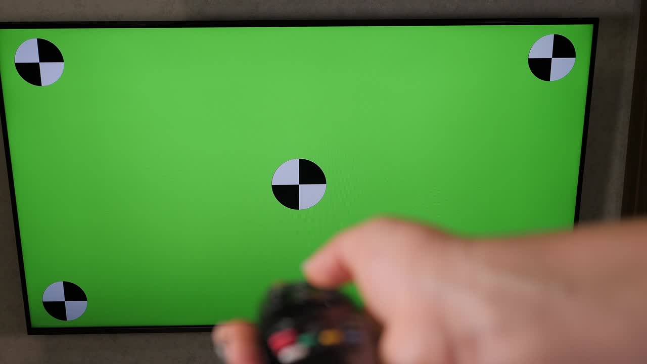 손으로 tv 리모컨을 들고 녹색 화면을 통해 현대적인 텔레비전 세트를 들고 있습니다.