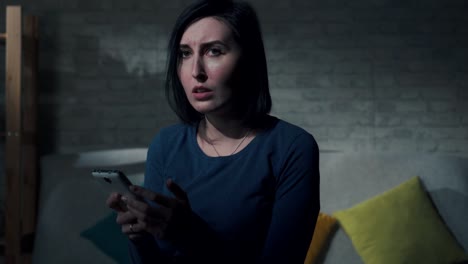 young woman with a phone in her hand learns the sad news while sitting in a dark room