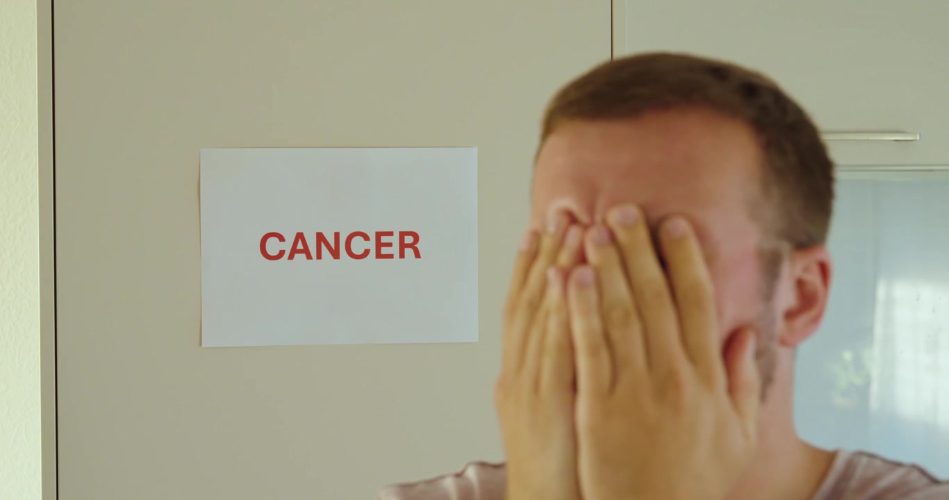 Descrizione: Uomo che si copre il viso con le mani e scuote la testa dopo la notizia del cancro, mostrando tristezza, paura e disagio emotivo.