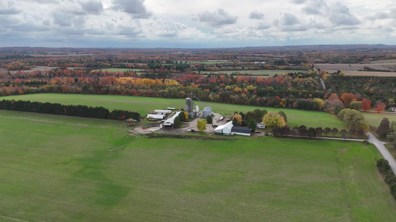 Fredfyldt luftfoto af en landbrugsejendom omgivet af levende efterårsløv og frodige grønne marker under en skyet himmel, Port Hope, Ontario, Canada.