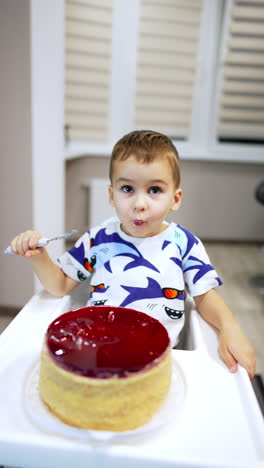 beautiful baby boy sitting at high chair in front of a bog cake. high angle view at the child enjoying sweet dessert. vertical video.