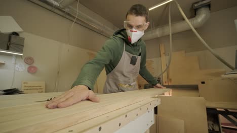 woodworker professional in mask and glasses checks wood raw, wooden plank, plywood panel