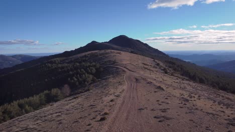 Aerial-shot-back-view-of-young-hiker-in-mountain-range-close-to-Madrid-during-afternoon-with-blue-sky-and-white-clouds