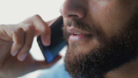 una foto de cerca de un hombre barbudo sonriente hablando en un teléfono inteligente.