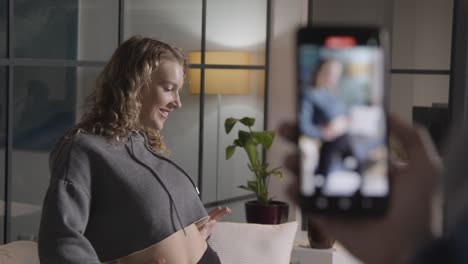 person recording social media video on mobile phone of woman dancing at home