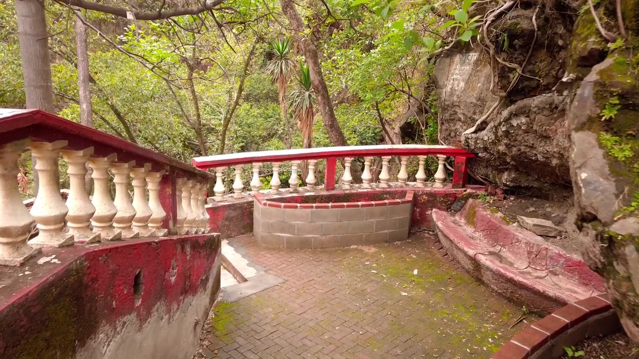 Sentiero in mattoni con balaustra rossa e bianca invecchiata, circondato da una foresta lussureggiante e alberi secolari vicino alla cascata Tallersigueros in Messico, di giorno