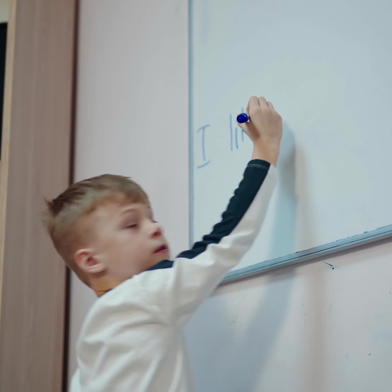 Boy studying at school. Schoolboy writing on a whiteboard with a marker in the classroom. Elementary education.