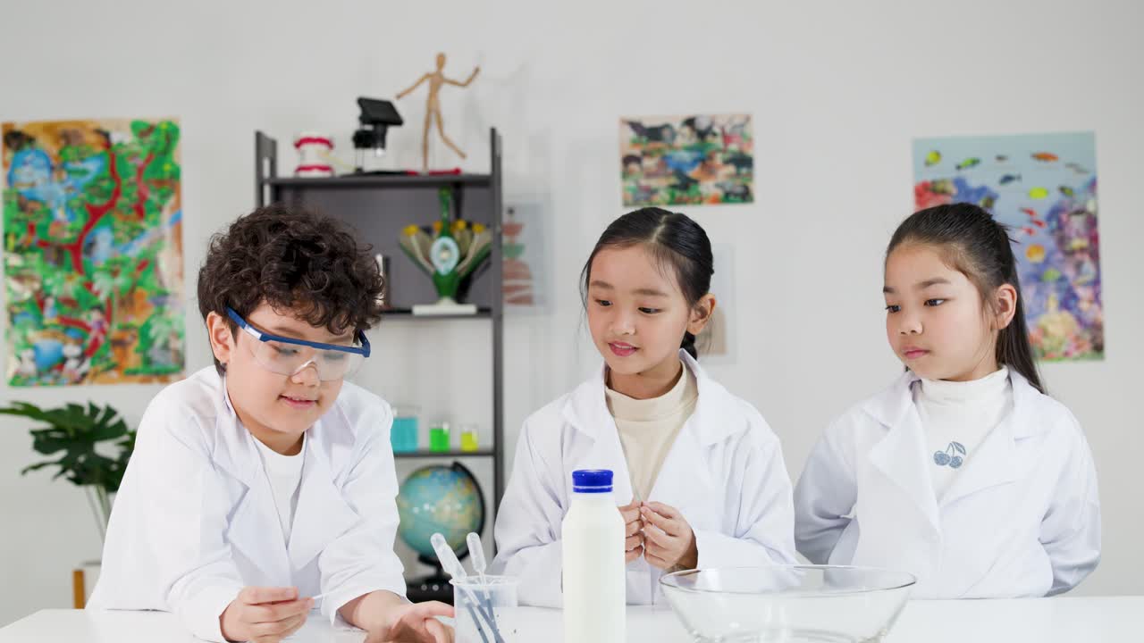 白衣と安全ゴーグルを着用した3人のアジア系の子供たちが、一緒に科学実験を行っている。