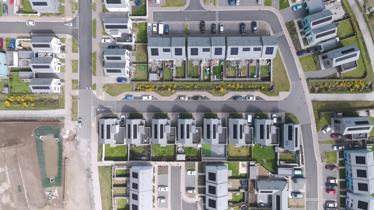 Precise aerial of high-density new-build estate of flat-roof solar homes, symmetric streets, parked cars and communal greens demonstrating compact eco-urban planning