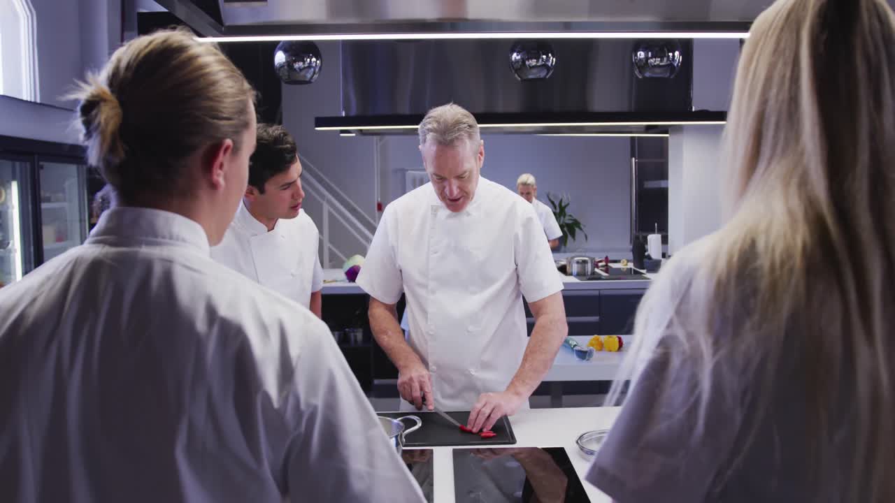 cocinero caucásico profesional en una cocina de un restaurante que enseña a un grupo de chefs aprendices