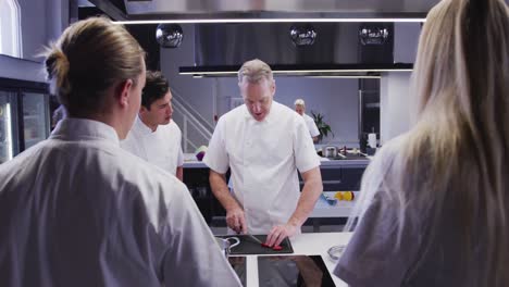 cocinero caucásico profesional en una cocina de un restaurante que enseña a un grupo de chefs aprendices