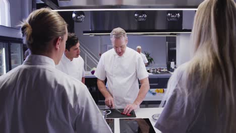 professional caucasian male chef in a restaurant kitchen teaching a group of trainee chefs