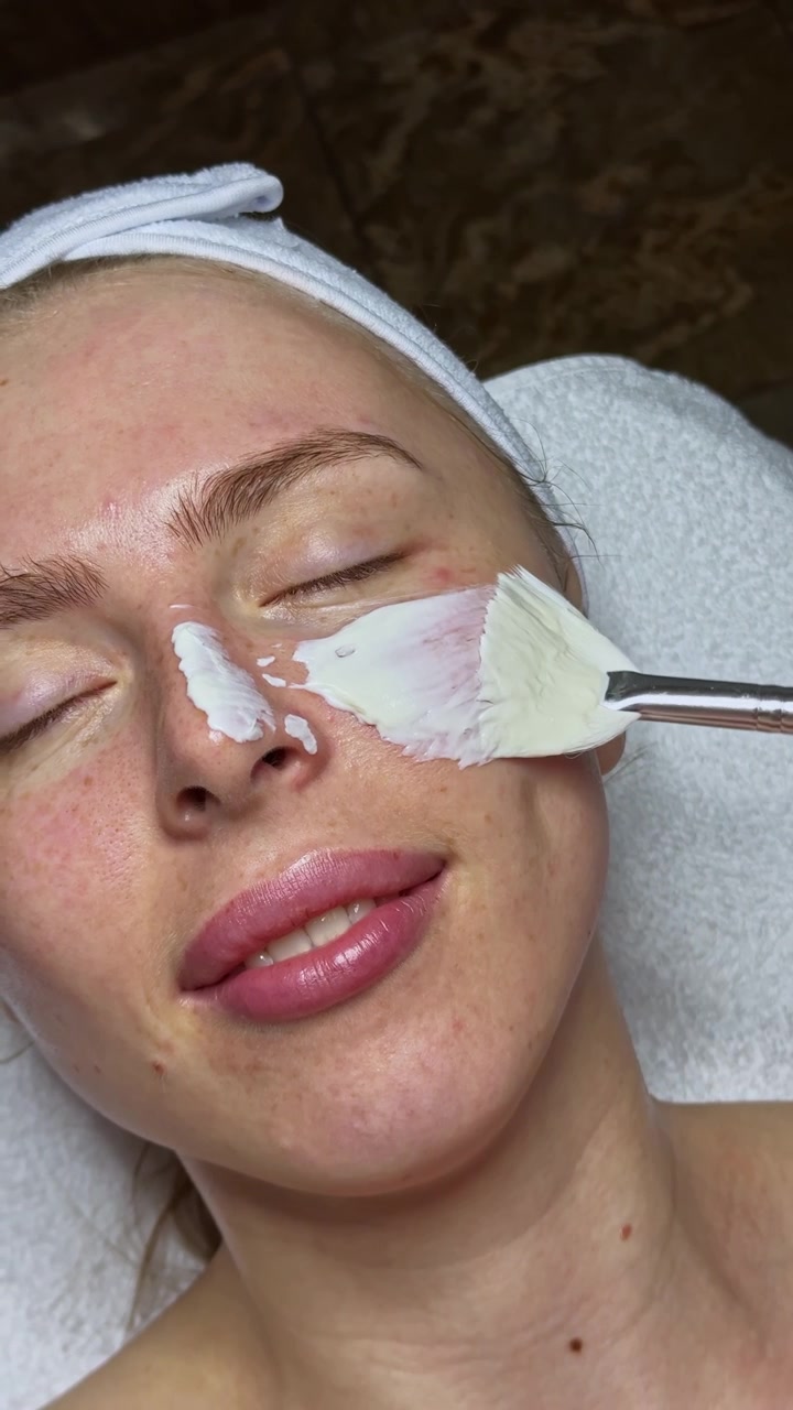 Donna che riceve un trattamento viso in una spa nel pomeriggio con una crema bianca applicata sul viso.