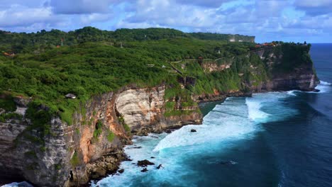 astounding uluwatu cliffs and ocean waves on a cloudy day with uluwatu temple in distance at bali in indonesia