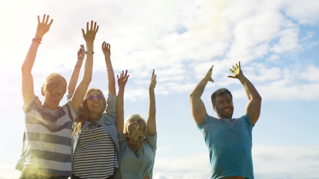 un grupo multiétnico de jóvenes diversos salta y lanza polvo de colores en el aire en la celebración del festival de holi. se divierten enormemente en este día soleado.