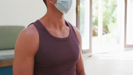 hombre caucásico con máscara facial en clase de yoga escuchando al instructor