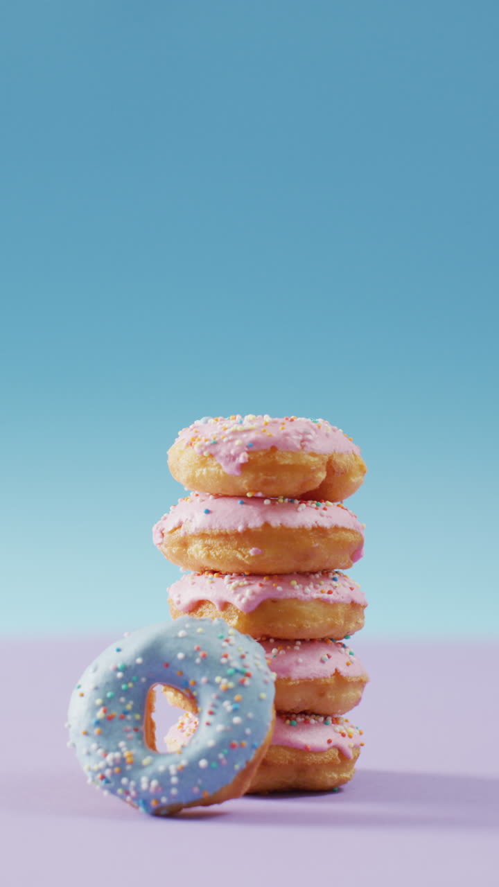 video vertical de una pila de rosquillas con glaseado rosa y azul sobre un fondo rosa y azul