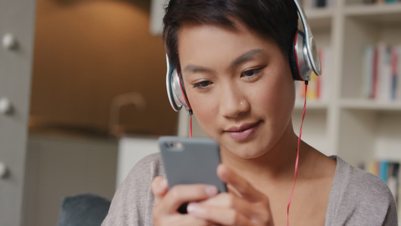 Bella donna asiatica a casa che ascolta musica sul suo smartphone.