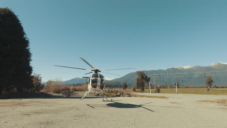 A-Small-Private-Helicopter-on-a-Large-empty-Take-Off-Pad-With-Spinning-Blades-Preparing-for-Takeoff---Handheld-Shot