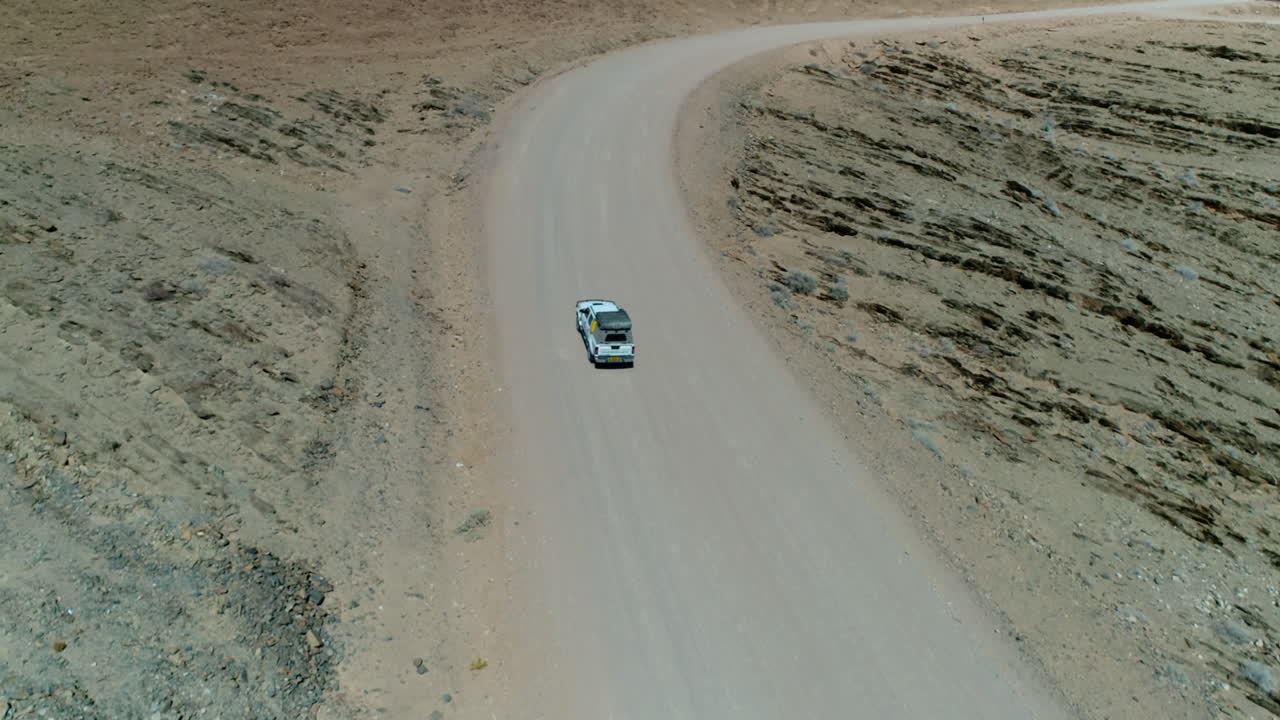 Aerial of a Jeep with roof tent driving on a gravel road in Namibia
