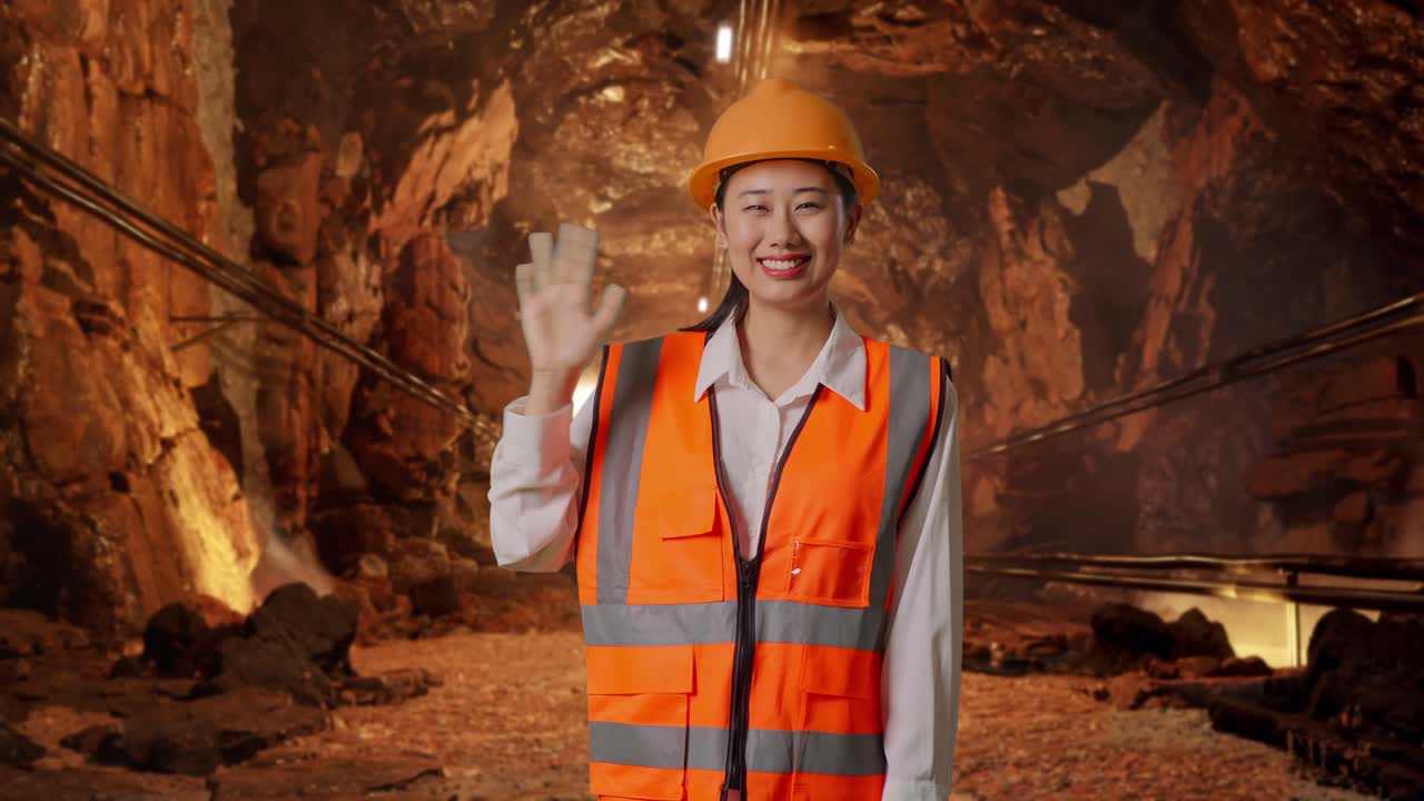Asian Female Engineer With Safety Helmet Smiling To Camera And Waving Hand Saying Bye In Underground Mine Tunnel
