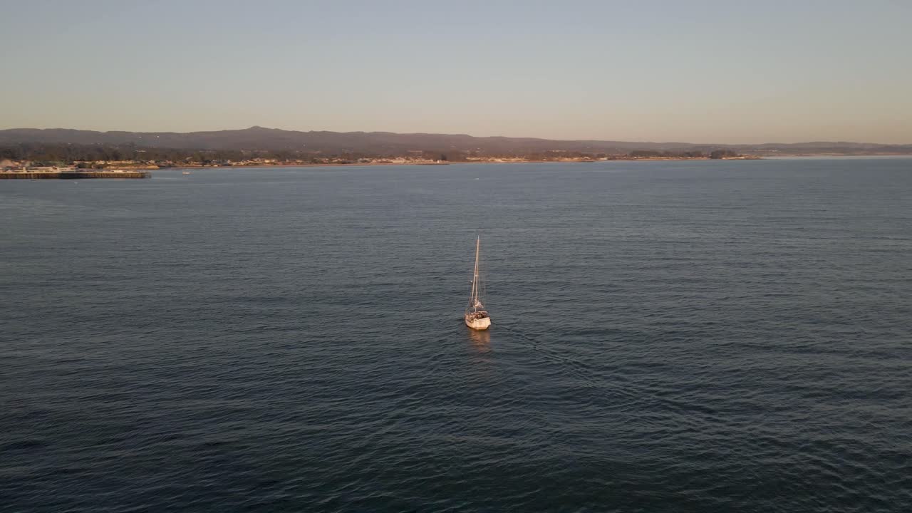 Near sunset, this captivating drone footage circles around a boat elegantly maneuvering into the dock in Santa Cruz, California, casting a serene ambiance over the scene