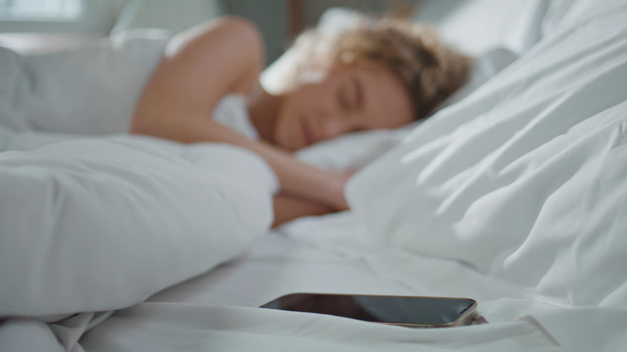 Kvinde vågner i hyggelig seng derhjemme. Nærbillede af hånd, der slukker vækkeur om morgenen.