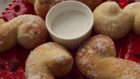 Camera-moving-over-a-setup-for-food-photography,-freshly-baked-Christmas-buns-with-sugar-and-raisins-on-an-ornate-red-plate