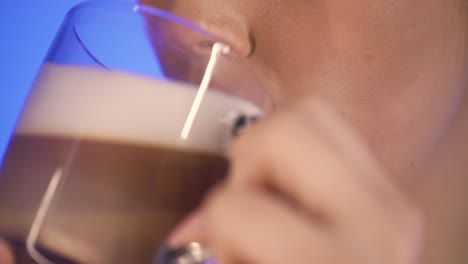 primer plano extremo de una mujer bonita mientras disfruta de un café latte macciato o capuchino recién preparado por la mañana para el desayuno y sonriendo felizmente frente al fondo azul en cámara lenta